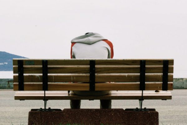 person wearing grey and orange hoodie sitting on brown wooden park bench during daytime